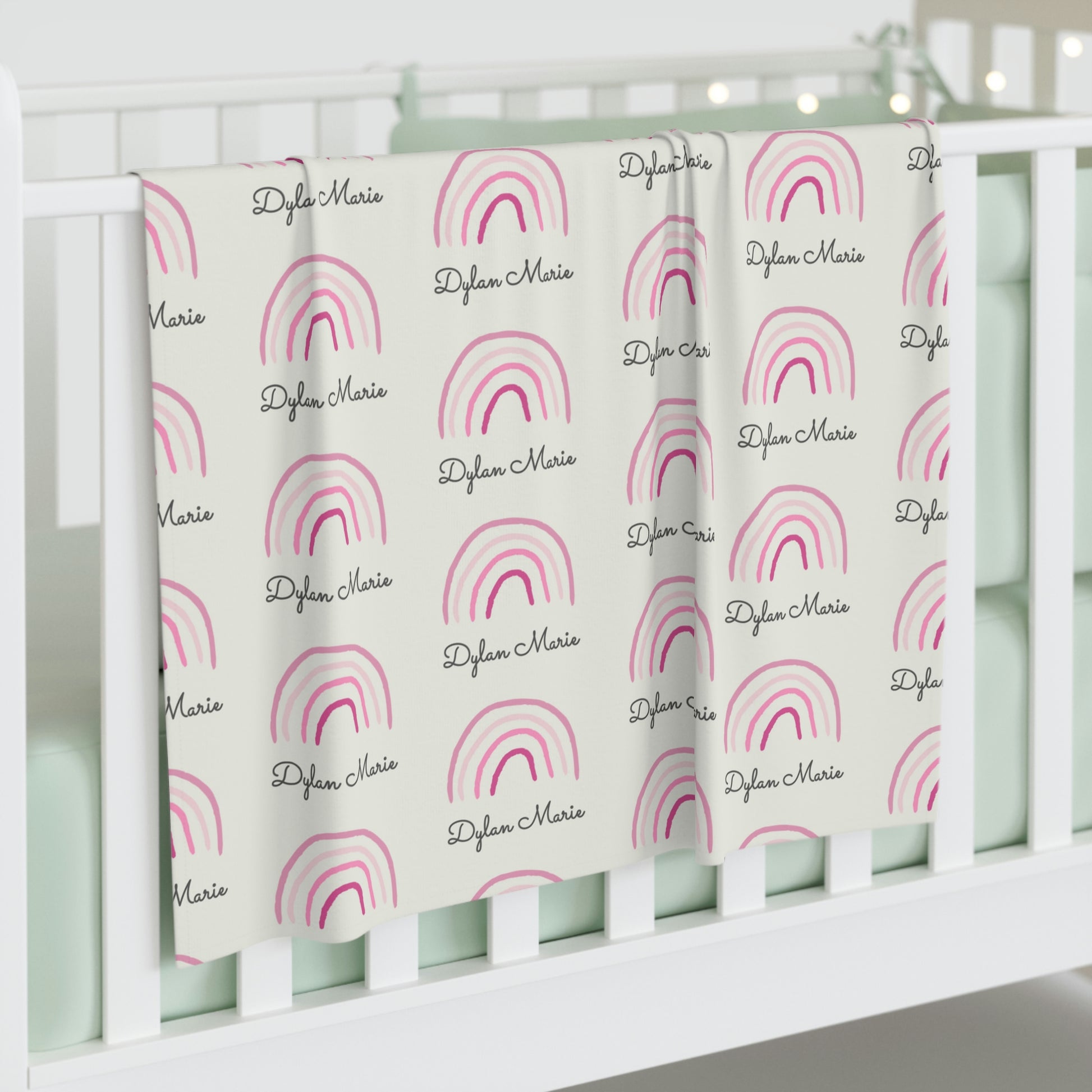 Jersey personalized baby blanket in pink rainbow pattern hung over side of white crib