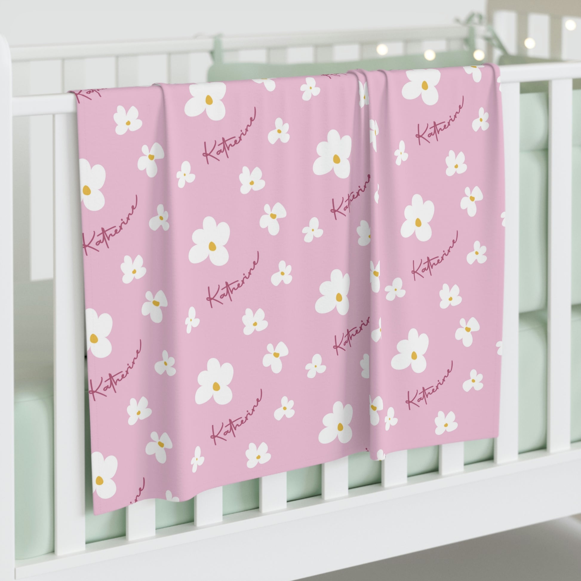 Jersey personalized baby blanket in pink daisy pattern hung over side of white crib