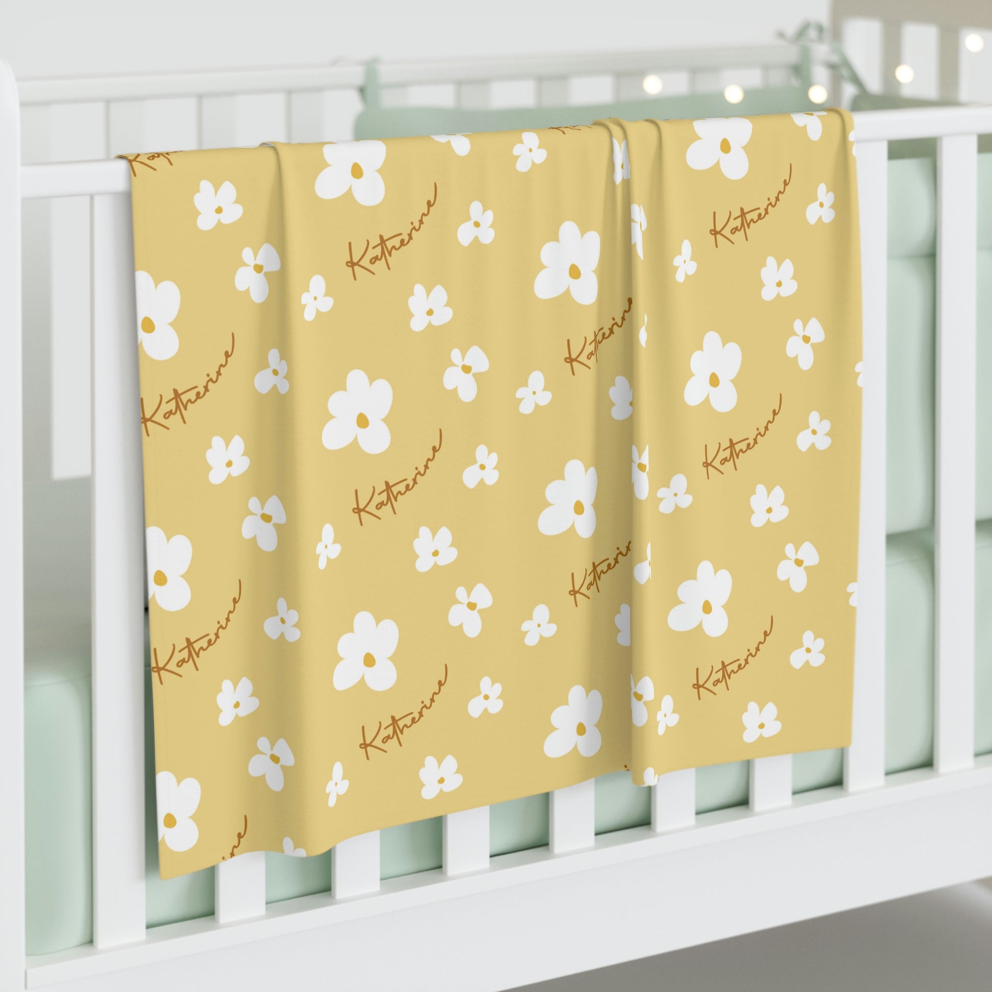 Jersey personalized baby blanket in yellow daisy pattern hung over side of white crib