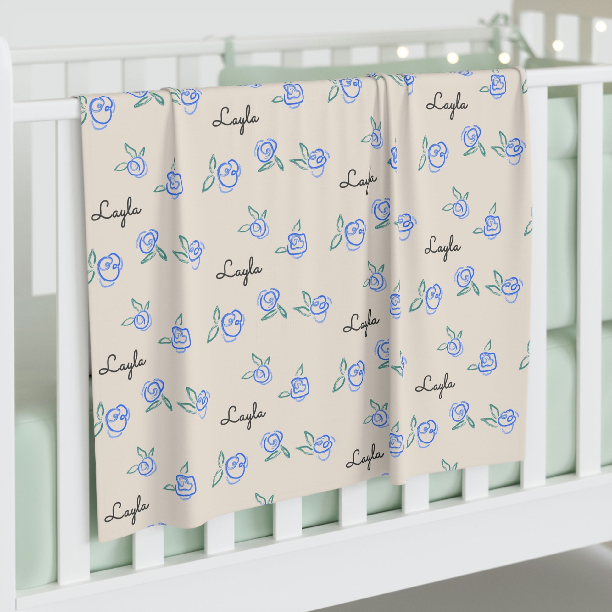 Jersey personalized baby blanket in blue rose pattern hung over side of white crib