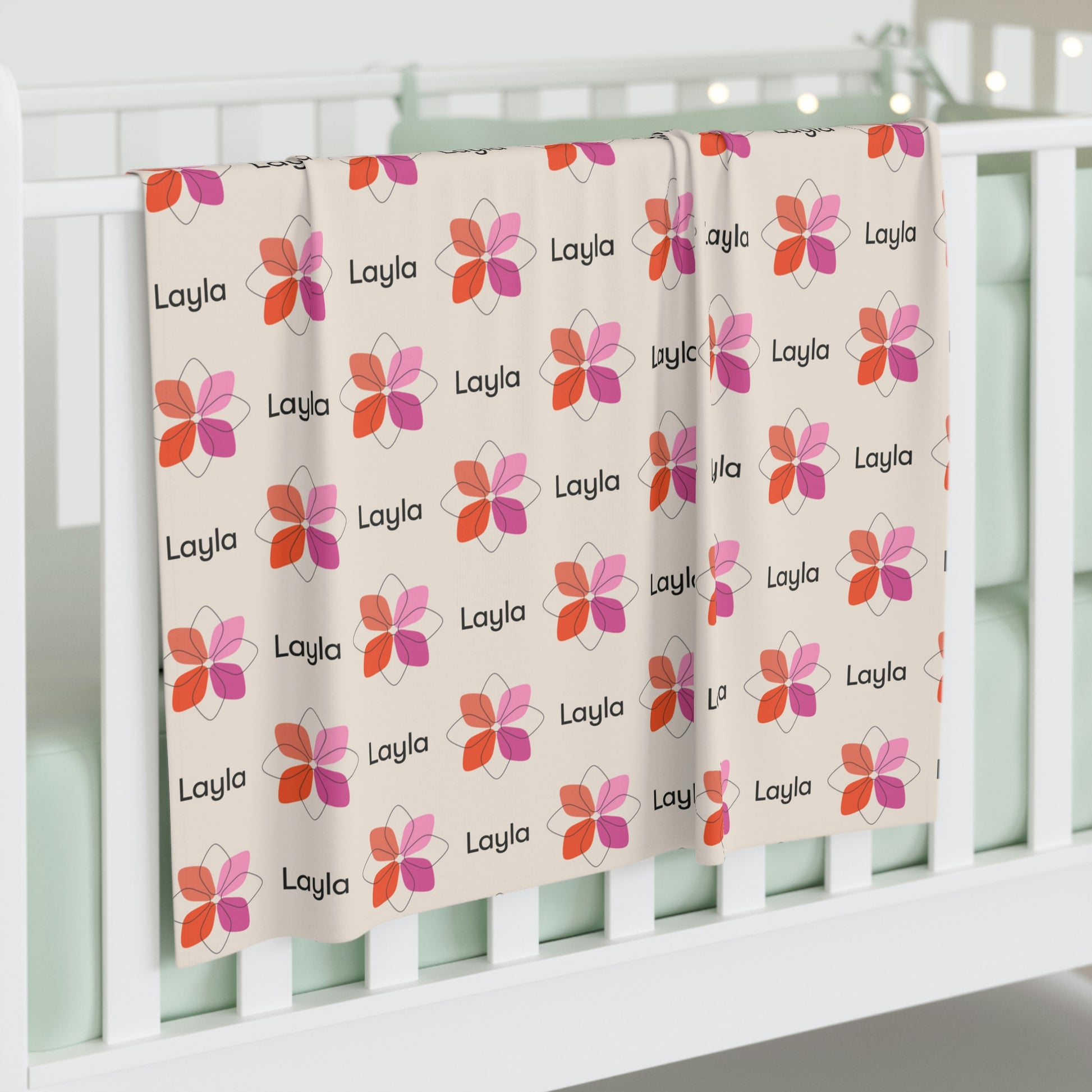 Jersey personalized baby blanket in pink boho geometric flower pattern hung over side of white crib