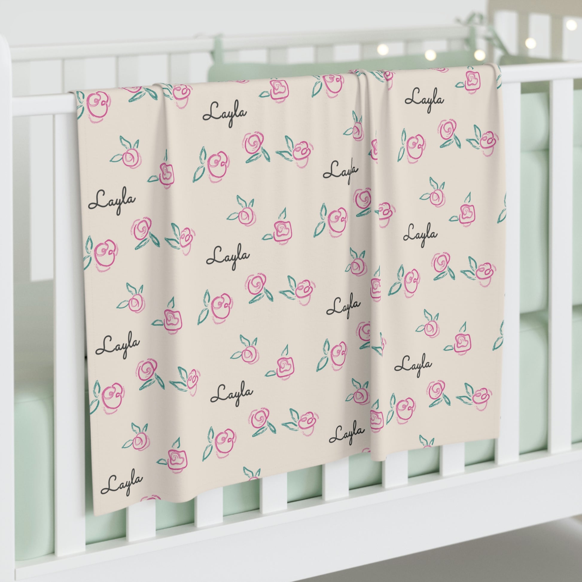 Jersey personalized baby blanket in pink rose with green leaves pattern hung over side of white crib