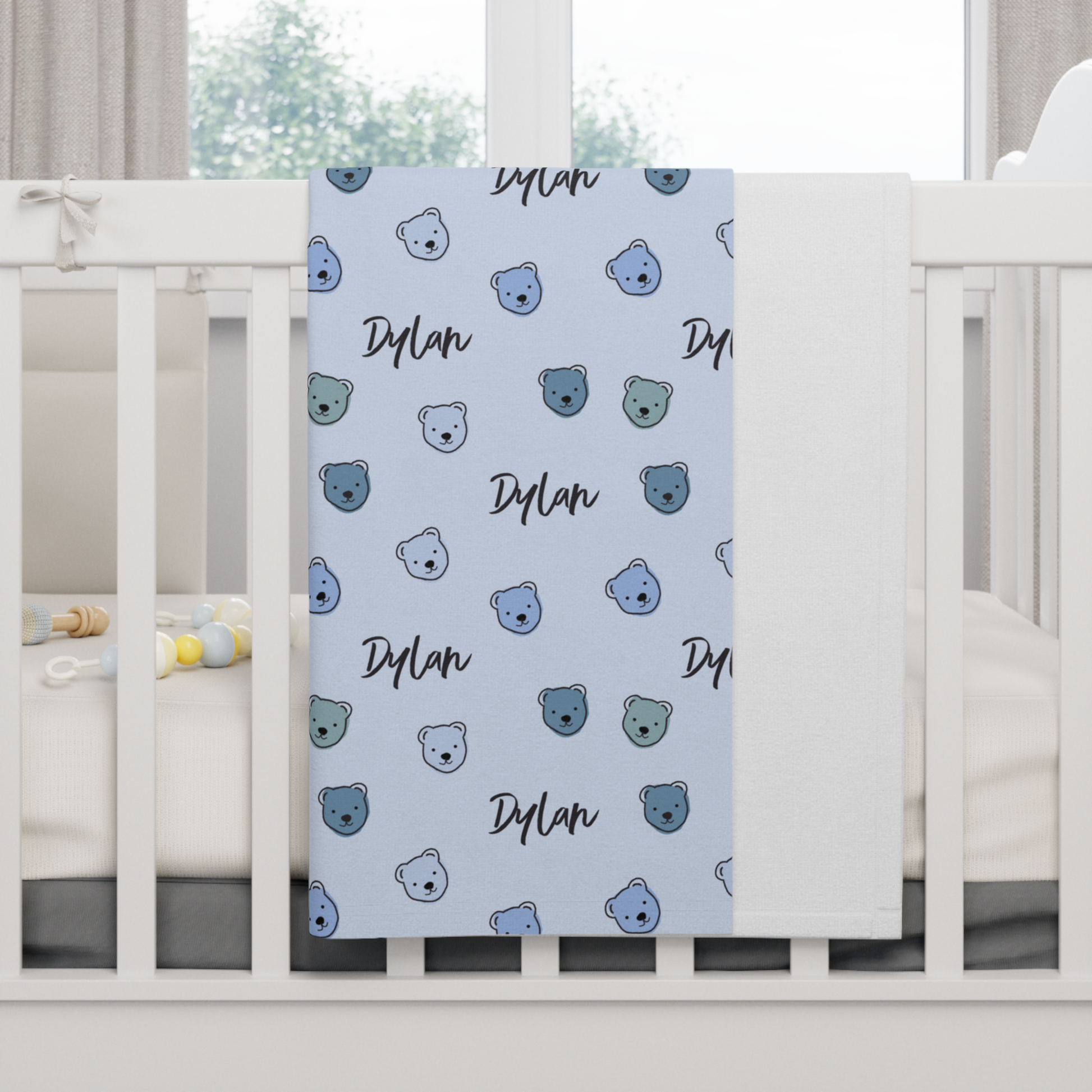 Fleece personalized baby blanket in blue cuddly bear pattern hung over side of white crib with window in the background