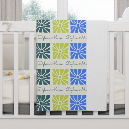 Fleece personalized baby blanket in boho blue flower pattern hung over side of white crib with window in the background