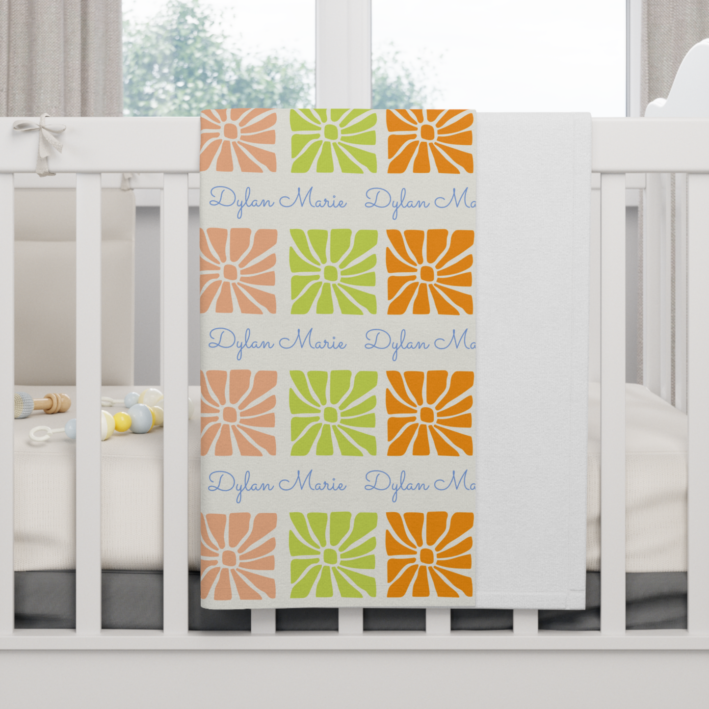 Fleece personalized baby blanket in a multi-colored boho flower pattern hung over side of white crib with window in the background