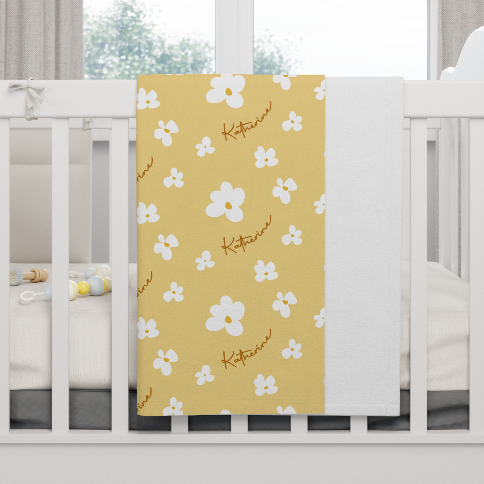 Fleece personalized baby blanket in yellow daisy pattern hung over side of white crib with window in the background