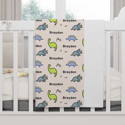 Fleece personalized baby blanket in dinosaur pattern hung over side of white crib with window in the background