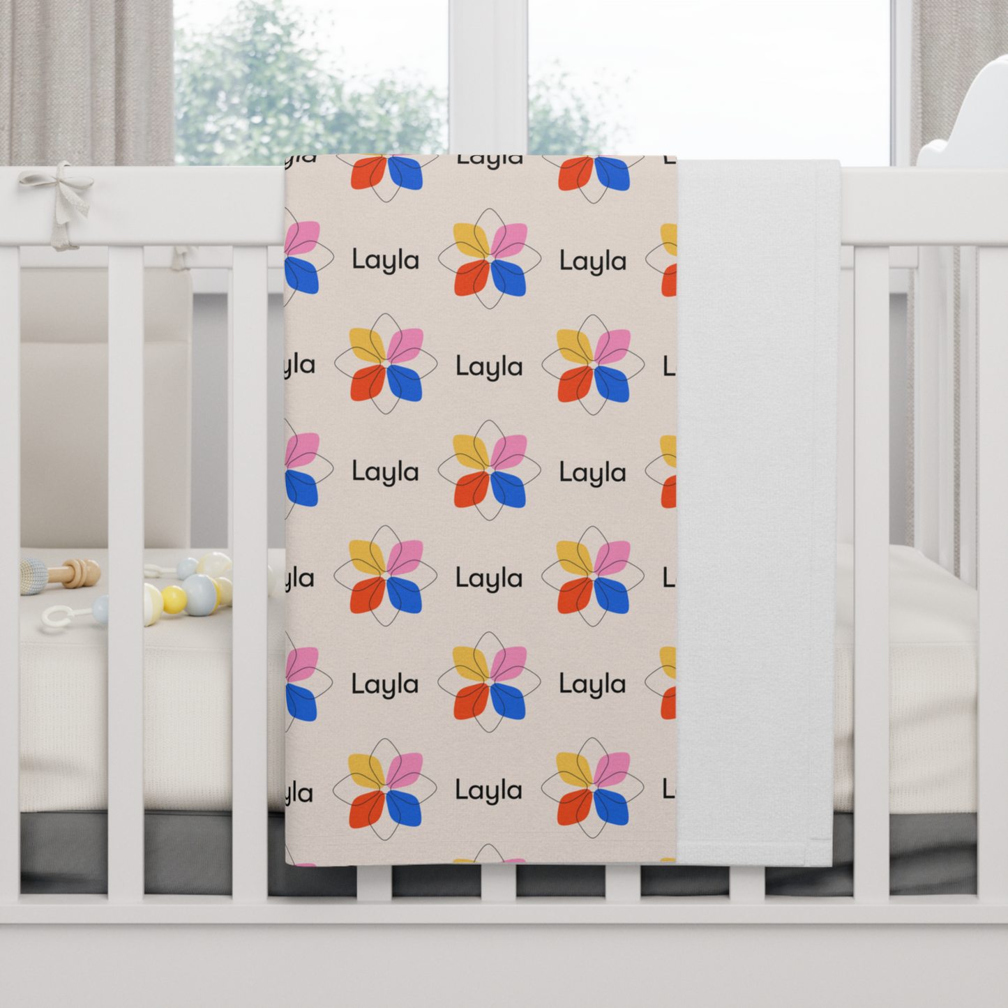 Fleece personalized baby blanket in a multi-colored boho geometric flower pattern hung over side of white crib with window in the background