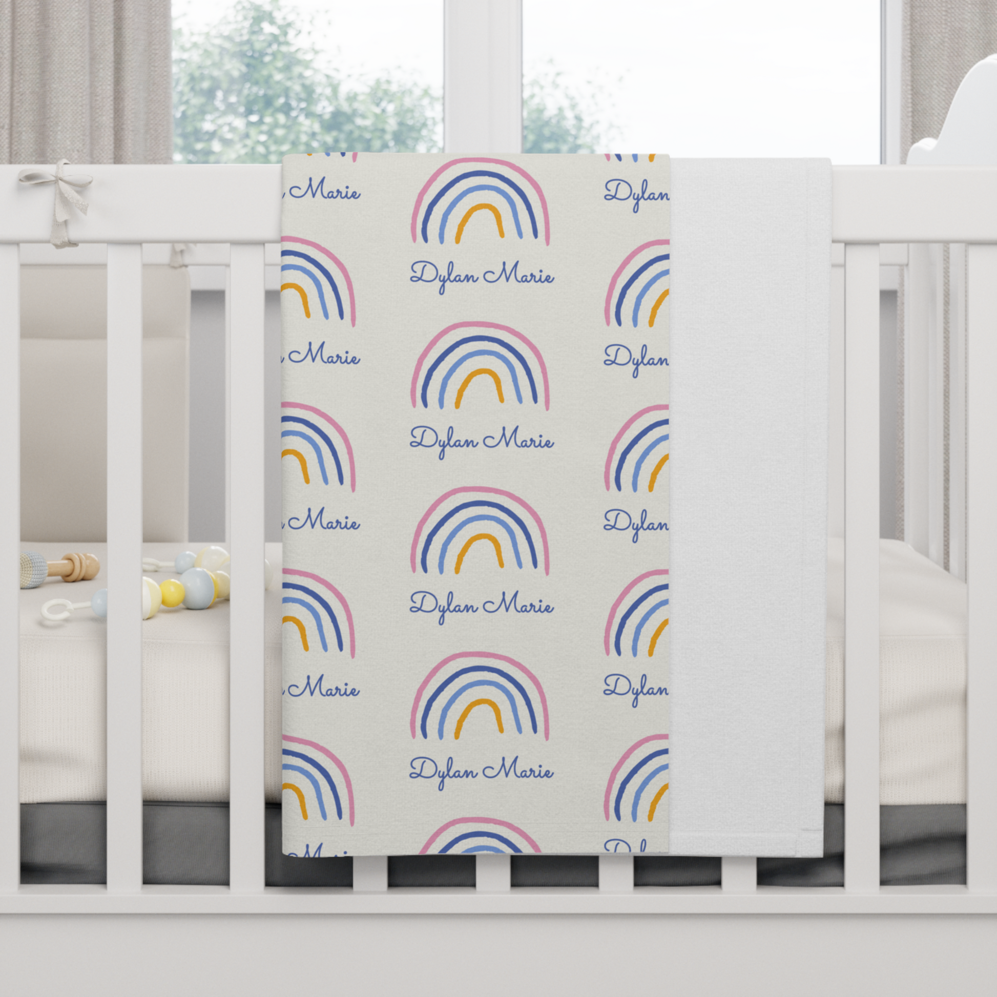 Fleece personalized baby blanket in rainbow pattern hung over side of white crib with window in the background