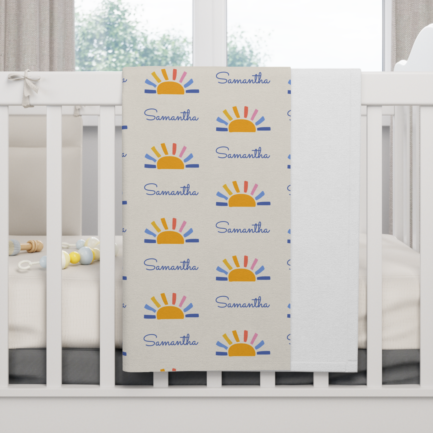 Fleece personalized baby blanket in sun pattern hung over side of white crib with window in the background