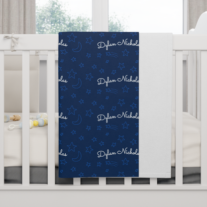 Fleece personalized baby blanket in stars and moon pattern hung over side of white crib with window in the background