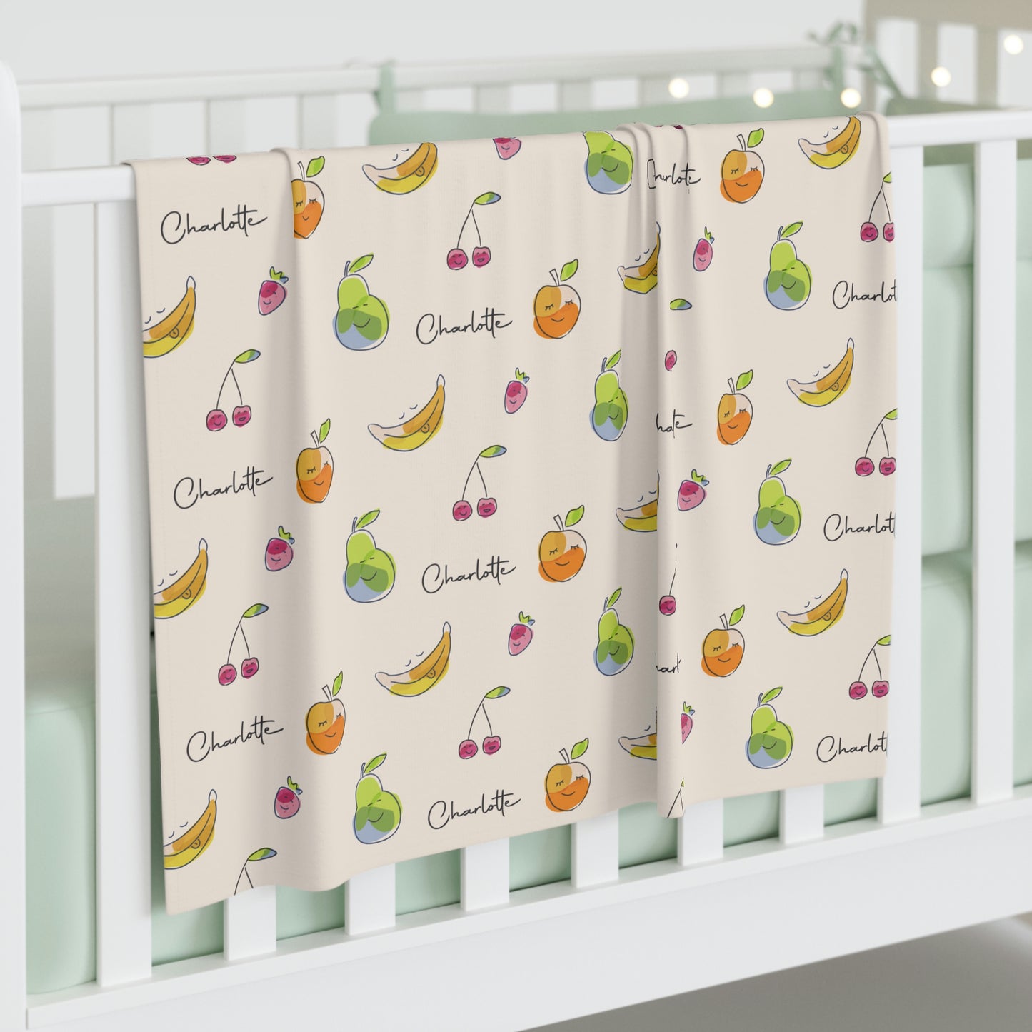 Jersey personalized baby blanket in happy fruit pattern hung over side of white crib