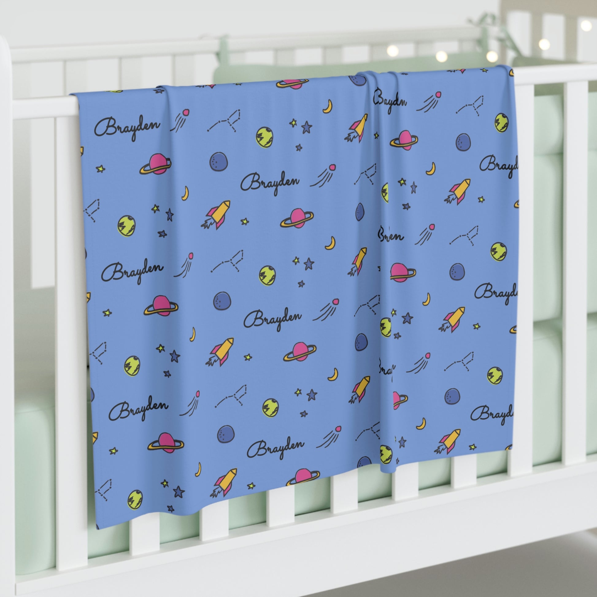 Jersey personalized baby blanket in space, rocket and stars pattern hung over side of white crib