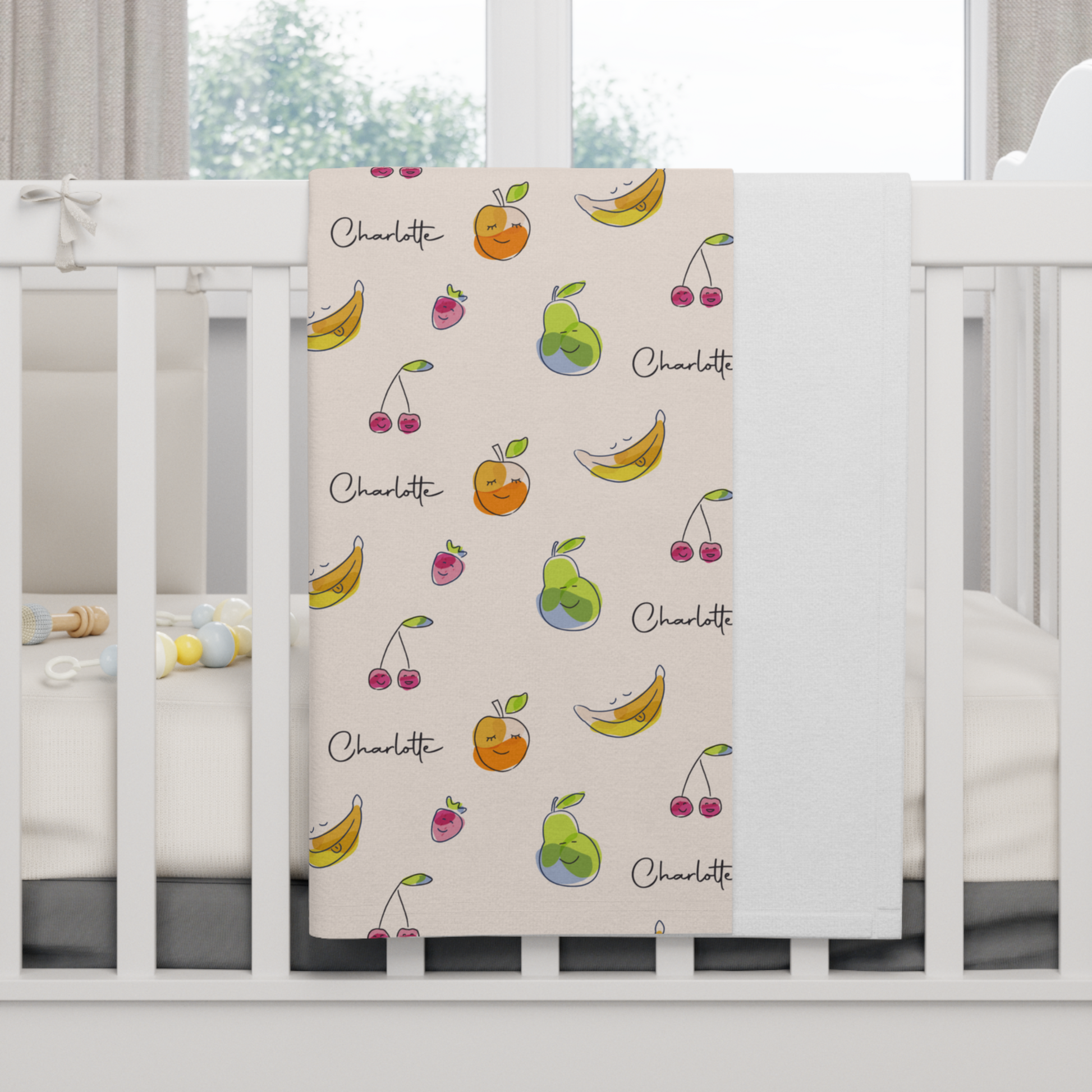 Fleece personalized baby blanket in happy fruit pattern hung over side of white crib with window in the background